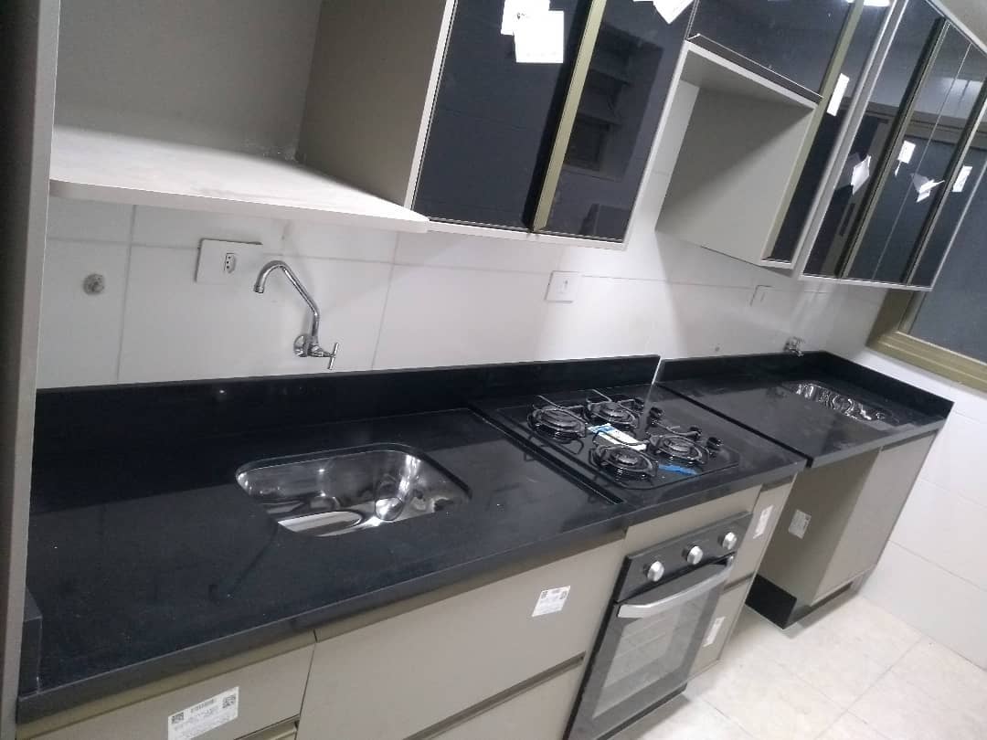 Cozinha com bancada preta, cuba inox, cooktop e armários suspensos